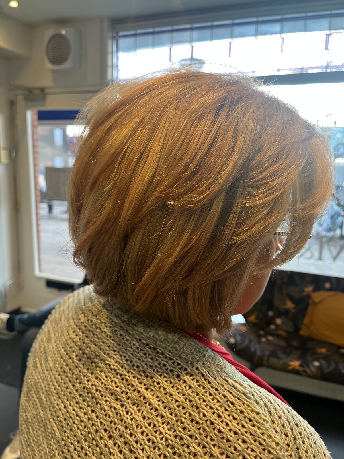 Damesmodel in koperblond van achteren, bij het raam van de salon